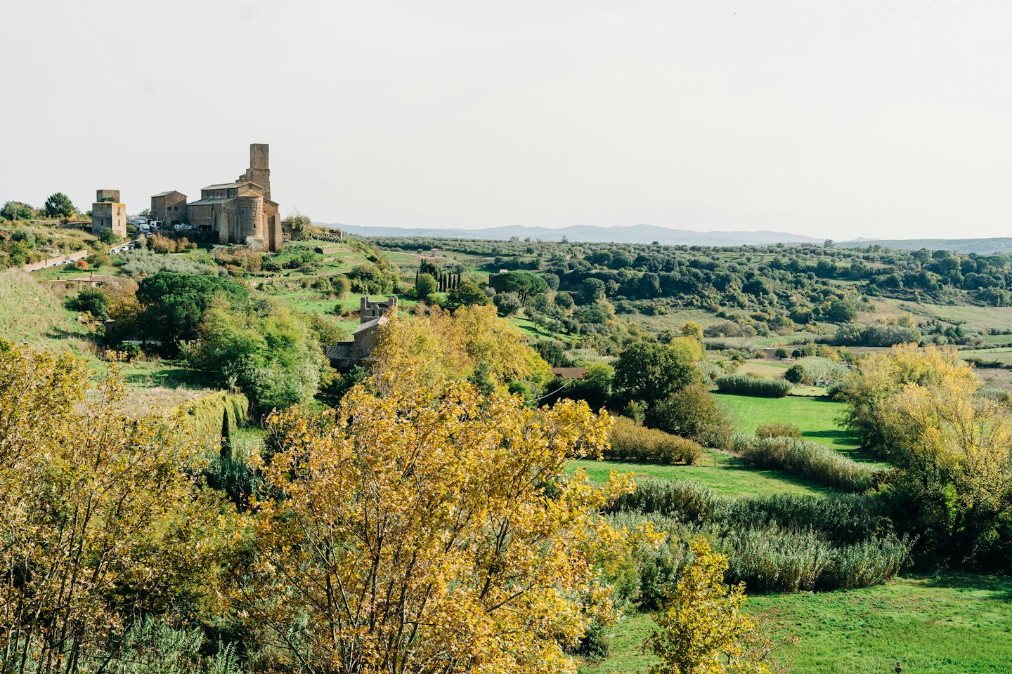 Antica città in pietra con torri su una collina verde.