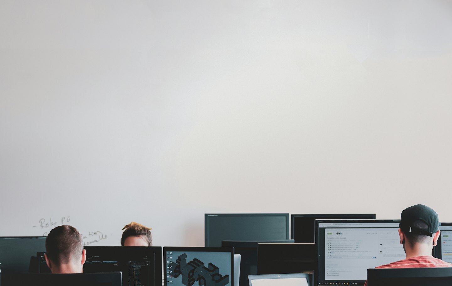 Tre professionisti che lavorano al computer su una parete bianca.
