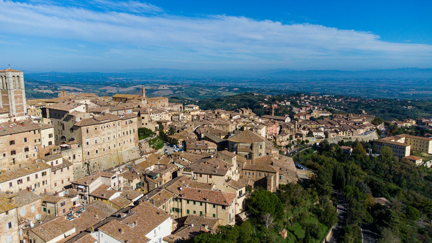 Borgo storico in pietra con tetti in cotto che domina la campagna.