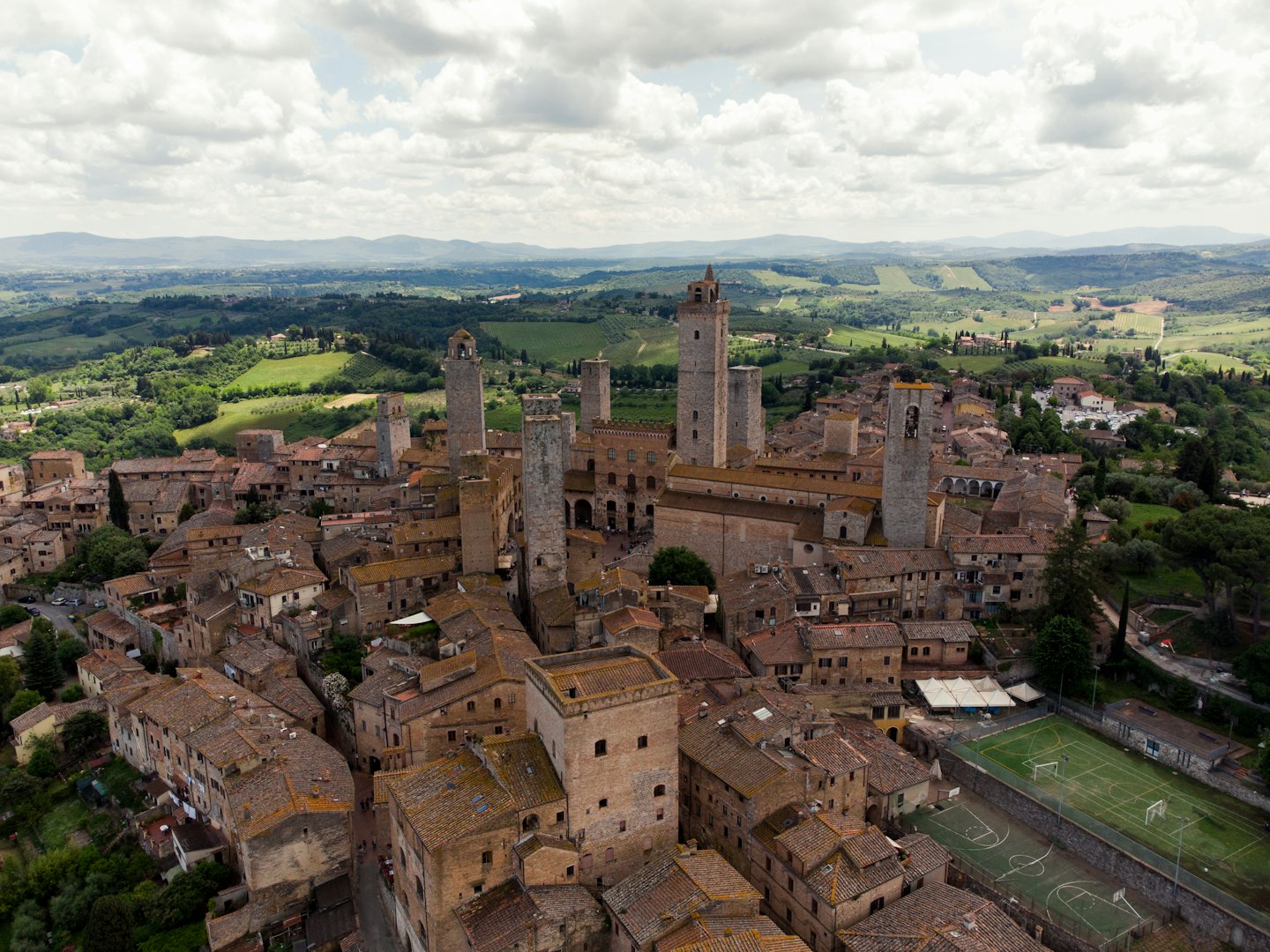 Torri medievali di pietra si ergono sopra i tetti di terracotta di un borgo collinare.